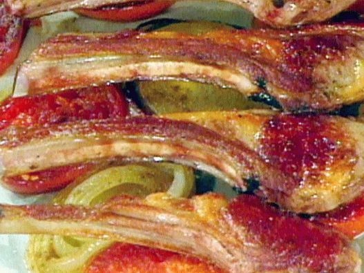 Foto von einem Lammkarree auf einem Kissen aus scharfen Tomaten und Zwiebeln